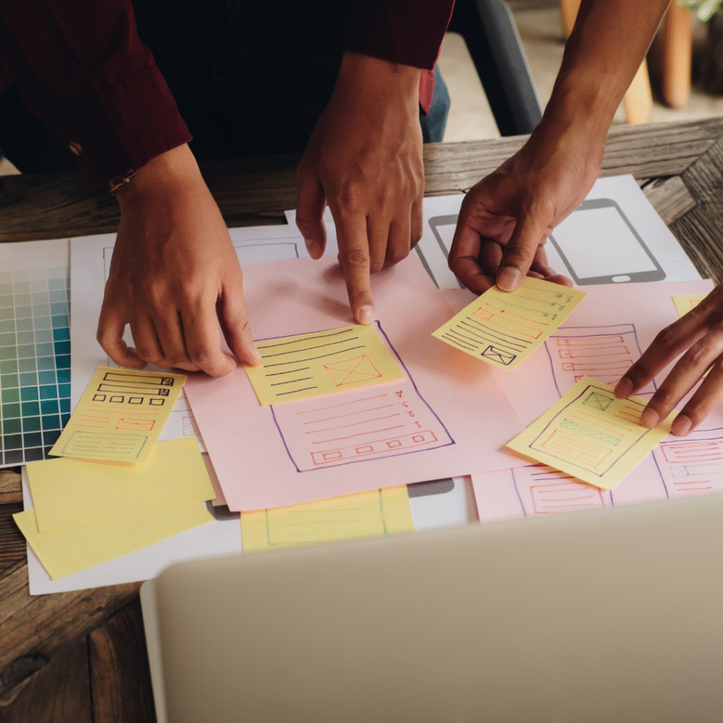 Hands collaborating on digital marketing strategy with sticky notes and sketches on a table, emphasizing teamwork and creative planning for small to mid-sized business growth.